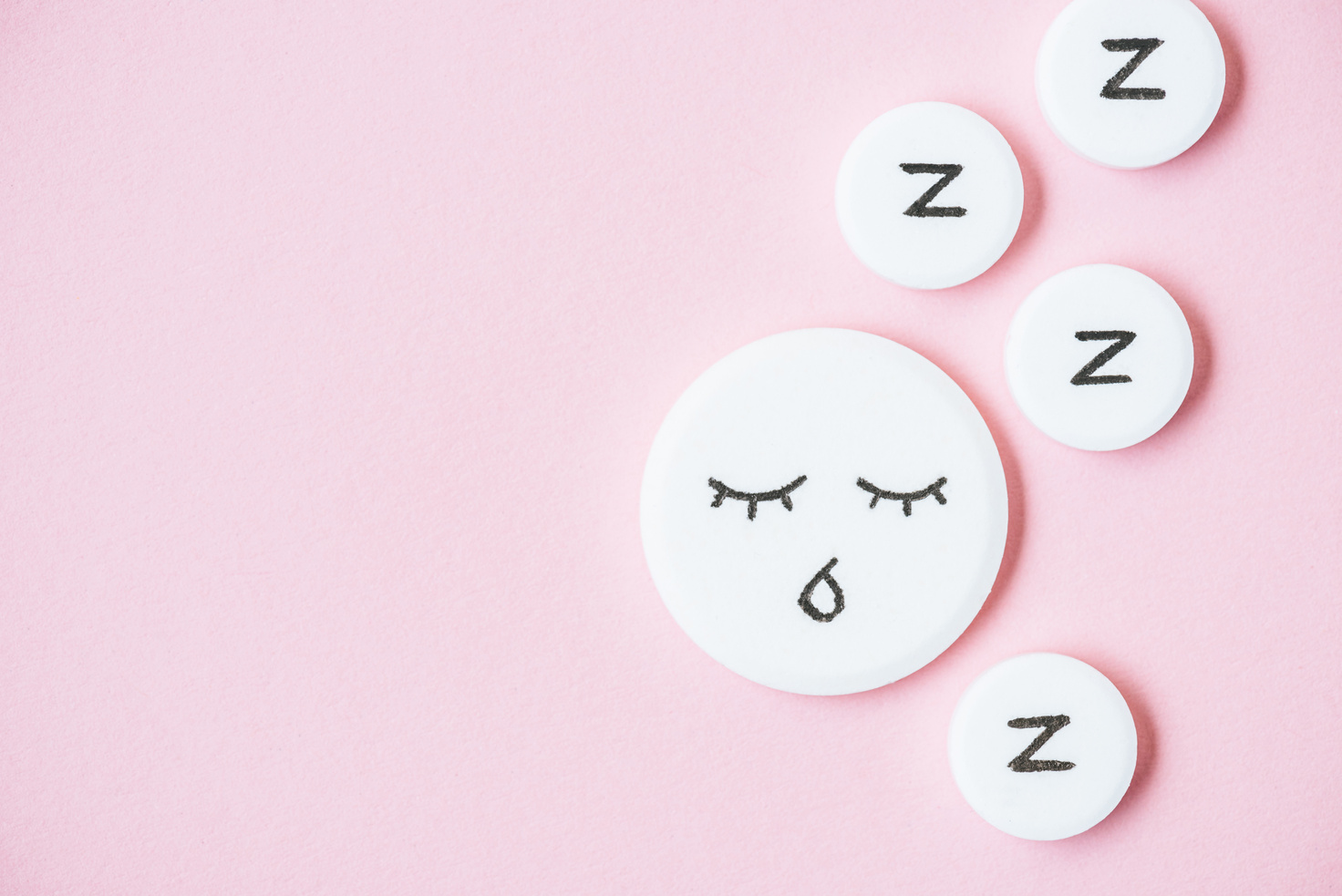 top view of sleeping pills with drawn face and Z signs on pink